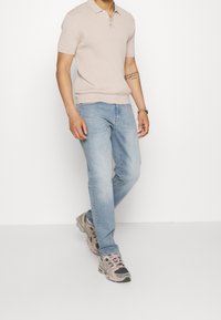 Polo shirt a maglia di un beige chiaro con maniche corte, abbinato a jeans in denim azzurro chiaro e sneakers grigie con dettagli rosa.