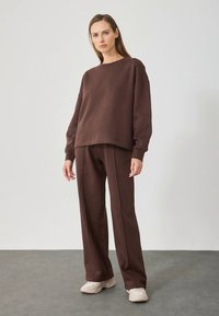 Brun croppad sweatshirt och matchande vida byxor i mjukt tyg. Outfitten har en avslappnad passform och minimala söm detaljer.