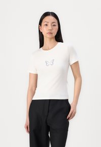 T-shirt blanc à manches courtes avec un imprimé de papillon bleu au centre. Le tissu est lisse et ajusté, avec un col rond classique.
