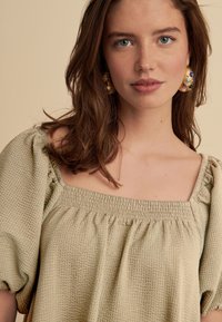 Hellolivgrünes, gewebtes Oberteil mit quadratischem Ausschnitt, Puffärmeln und gerafften Details entlang des Ausschnitts. Klassischer, strukturierter Stoff.