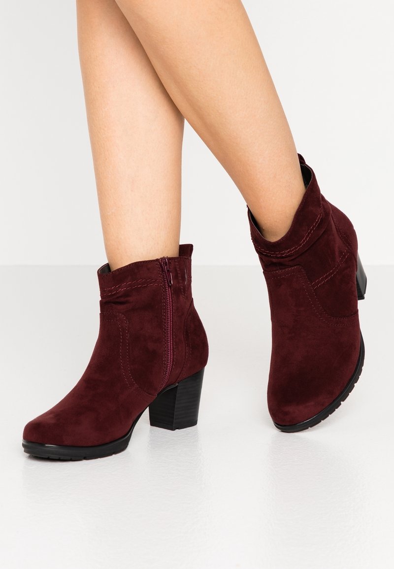 Burgundowe zamszowe botki za kostkę z tłoczoną piętą, bocznym zamkiem błyskawicznym i przeszyciami. Gładka tekstura z zaokrąglonym noskiem.