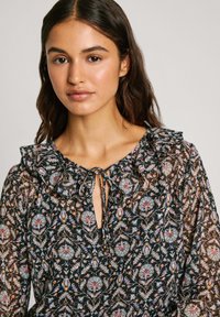 Blusa nera a fiori con scollatura arricciata, chiusura con cravatta e tessuto trasparente con motivi paisley e botanici multicolori.