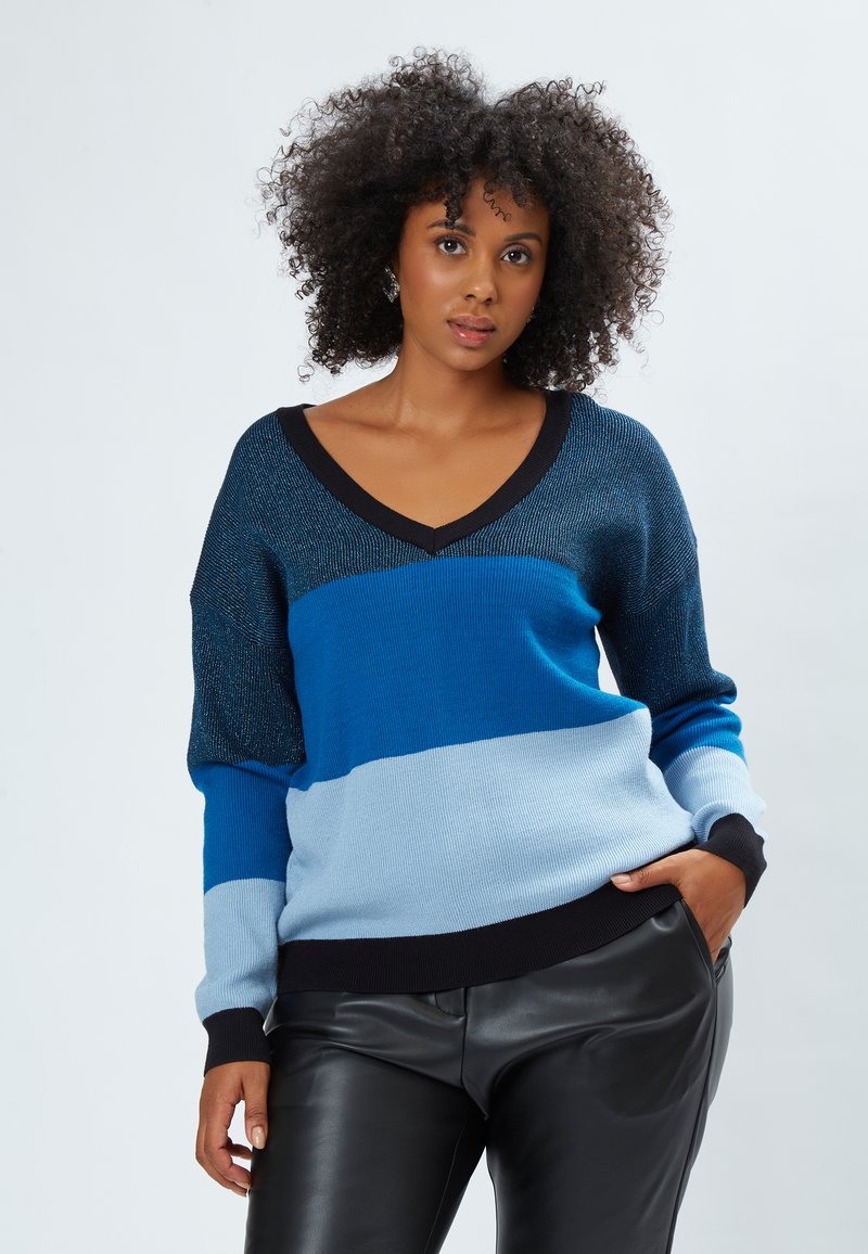 Suéter a rayas azul y celeste con cuello en V, textura de punto y acentos negros, combinado con pantalones de cuero negros.