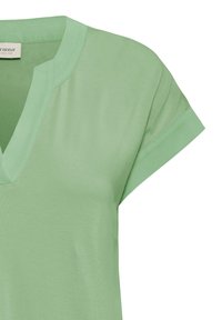 Chemise courte à manches courtes vert clair avec un col en V entaillé et des poignets de manches repliés, fabriquée en tissu doux et lisse.