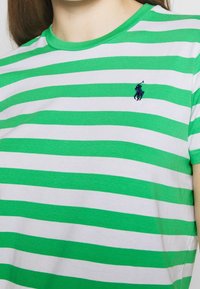 Persona que lleva una camiseta con rayas horizontales verdes y blancas y un pequeño logo bordado en azul marino de un jugador de polo en el pecho.