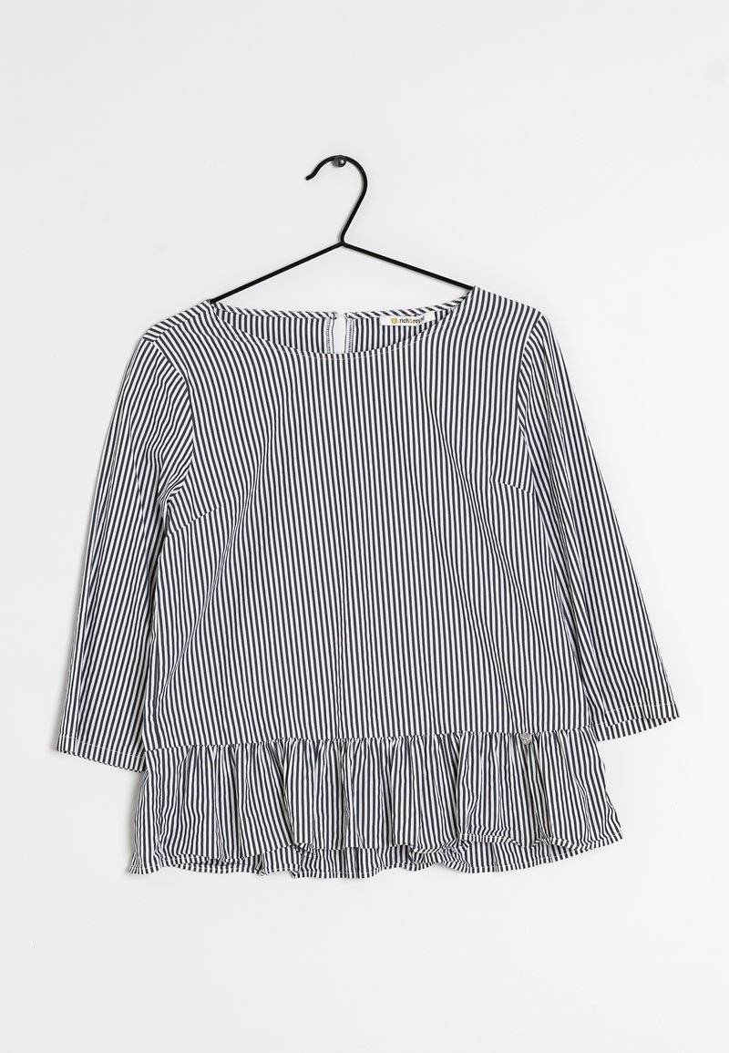 Randig långärmad topp i marinblått och vitt. Har en rund halsringning och en volangkant. Tillverkad av ett lätt tyg med en slät textur.