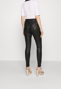 Pantalons en simili cuir noir au design épuré, avec un accent côtelé à la taille. Associés à des talons compensés argentés.