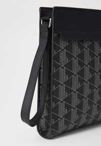 Sort syntetisk lædertaske med geometrisk mønster, justerbar rem og lynlås lukning. Har logodetalje og glat tekstur.