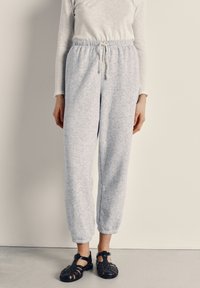 Gray, textured jogger pants with elastic waistband and drawstring, paired with black, strappy sandals featuring a closed toe design.