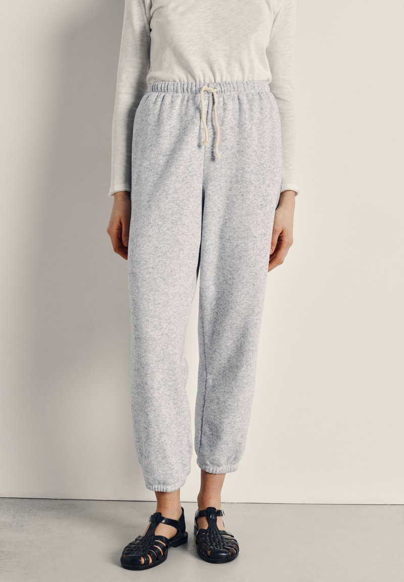 Gray, textured jogger pants with elastic waistband and drawstring, paired with black, strappy sandals featuring a closed toe design.