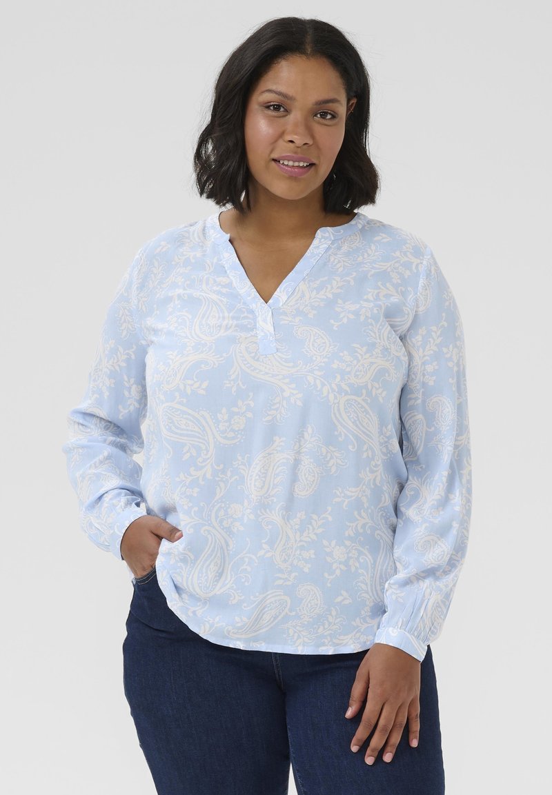 Blouse bleu clair avec un motif cachemire, dotée d'un col en V, de manches longues et d'accents de boutons aux poignets. Texture de tissu douce.