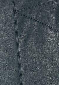 Pelle textured di un verde scuro con una grana visibile, caratterizzata da accenti cuciti geometrici in un motivo triangolare. Finitura durevole e liscia.