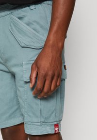 Ljusblå cargoshorts i bomullsblandning med stora framfickor, detalj med röd etikett och rak skärning.