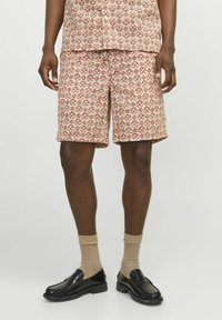 Shorts à motifs en terre cuite et crème, fabriqués en tissu léger. Dotés d'un imprimé géométrique et d'une coupe décontractée, assortis à des mocassins noirs.