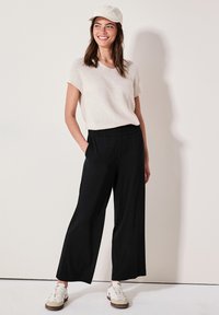 Lichtbeige korte mouwen gebreide top met een ronde hals, gecombineerd met zwarte wijde broek met elastische tailleband en zijzakken.
