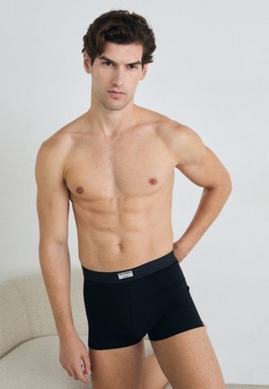 Boxer briefs neri con design aderente e cintura elasticizzata. Il materiale sembra liscio, con un'etichetta sulla cintura anteriore.