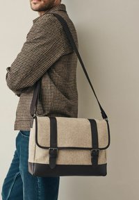 Beige wool bag with dark leather accents, a flap closure, and two adjustable straps. Rectangular shape, minimalistic design.
