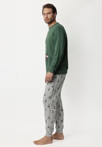 Sudadera verde de manga larga con estampado gráfico, combinada con pantalones de pijama grises que muestran un patrón juguetón con acentos.