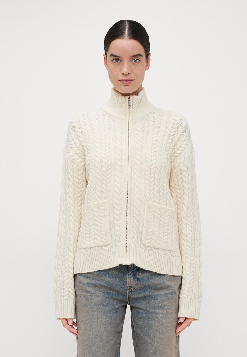 Πλέκτο κρεμ cardigan με ψηλό γιακά και πλήρη φερμουάρ, που διαθέτει σχέδια καλωδίων, δύο μπροστινές τσέπες και ριγωτές μανσέτες.