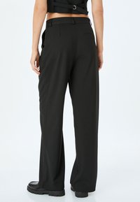 Pantaloni neri a gamba larga realizzati in tessuto morbido. Presentano una vita alta, una tasca posteriore e una silhouette pulita e sartoriale.