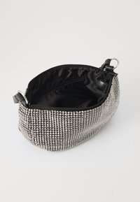 Bolso de mano de strass plateado con un interior de satén negro, cierre de cremallera, forma curvada y un anillo de metal adjunto a un lado.