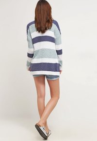 Pull rayé et duveteux en bleu sarcelle, marine et blanc. Manches longues, ourlet arrondi, texture douce et coupe ample. Associé à un short en jean et des chaussures métalliques.