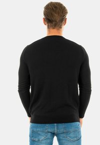 Schwarzer Strickpullover mit gerippten Akzenten, Rundhalsausschnitt und langen Ärmeln, getragen mit blauer Jeans, von hinten betrachtet.