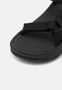 Juodos šlepetės su tekstūruota guma padais, minkštais dirželiais ir ergonomiška forma, sukurta komfortui ir palaikymui.