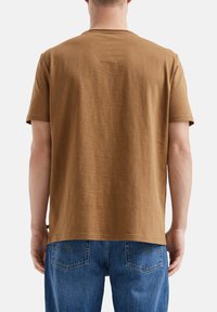 Brązowa koszulka z krótkim rękawem, wykonana z miękkiego materiału, o luźnym kroju i klasycznym dekolcie, pokazana z tyłu, bez wizualnych akcentów.