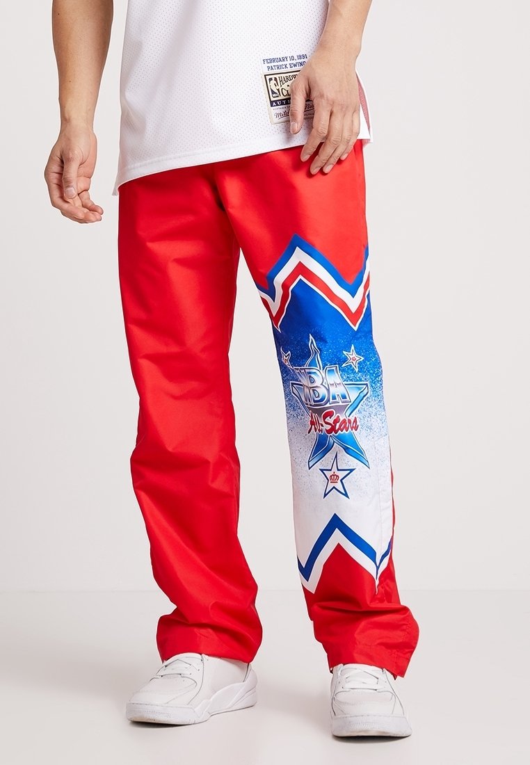 Pantalon en nylon rouge avec un motif graphique bleu et blanc comprenant des étoiles et le texte « NBA All-Stars » sur la jambe gauche. Texture lisse.