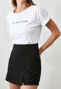 Mujer con una camiseta blanca que dice "QUIERO UN TICKET A CUALQUIER LUGAR" metida en una minifalda negra de cintura alta con aberturas frontales.