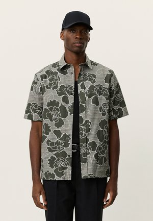 Kortærmet skjorte med krave i grøn med hvidt blomsterprint; letvægtsstof med en tekstureret finish; kombineret med en sort undertrøje og bukser.