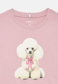 Light pink children's shirt with a white poodle illustration wearing a pink bow, labeled size EU 92 US 2T.