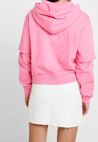 Sudadera corta rosa con capucha y cordones, material suave y puños acanalados, combinada con una falda de mezclilla blanca con bolsillos traseros.