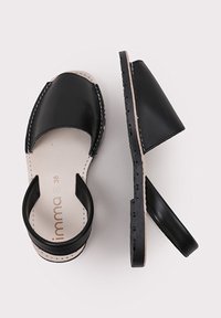Sandalias de cuero negro con punta redondeada y una correa alrededor del talón. Cuentan con plantillas de color beige y una suela de goma negra texturizada. Talla 38.
