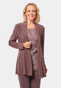 Lichte bruine cardigan over een gestippeld roze top, met lange mouwen en een open front ontwerp. De stof lijkt glad en heeft een relaxte pasvorm.