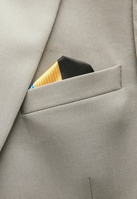 Tela de traje gris claro con un bolsillo afilado. Un pañuelo de bolsillo doblado presenta un diseño a rayas en amarillo, naranja y azul.