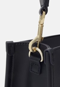 Marineblå skinnveske stropp med et gullfarget metallspenne. Funksjoner inkluderer en jevn tekstur og broderte detaljer på stroppfestet.