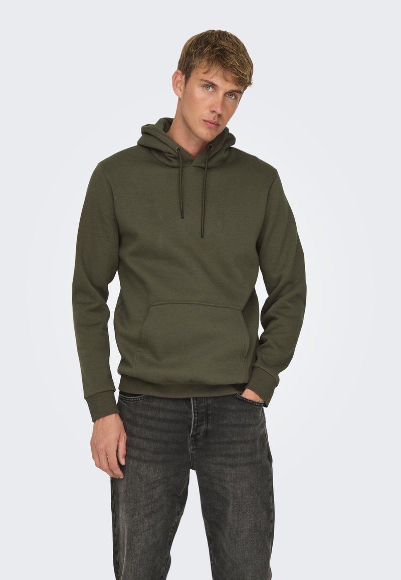 Sudadera verde caqui con un bolsillo tipo canguro, cordones ajustables y puños acanalados. Combinada con jeans de mezclilla gris oscuro.