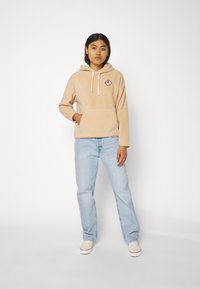 Beige, textured hooded sweatshirt with a front pocket and light pink drawstrings. Paired with light blue straight-leg jeans and white sneakers.