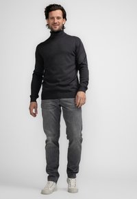 Czarny golf w ciemnoszarym kolorze o dopasowanym kroju, zestawiony z jasnoszarymi dżinsami i białymi sneakersami. Gładki materiał z ribbowanymi akcentami.