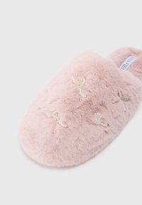 Pantufa rosa fofinha com laços de contas, textura suave, forma arredondada e um rótulo na lateral.