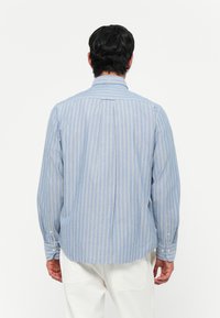 Blå og hvid stribet skjorte med lange ærmer, krave, knaplukning ved ærmerne og lige søm. Stoffet virker blødt og let.
