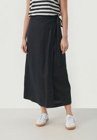 Black linen wrap skirt with a side tie and a straight silhouette, paired with white sneakers. Horizontal striped top visible above.