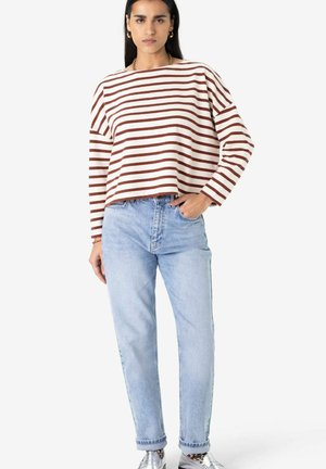 Haut à manches longues rayé crème et marron, associé à un jean bleu clair. Le haut présente un col large et une coupe décontractée. Chaussures argentées visibles.