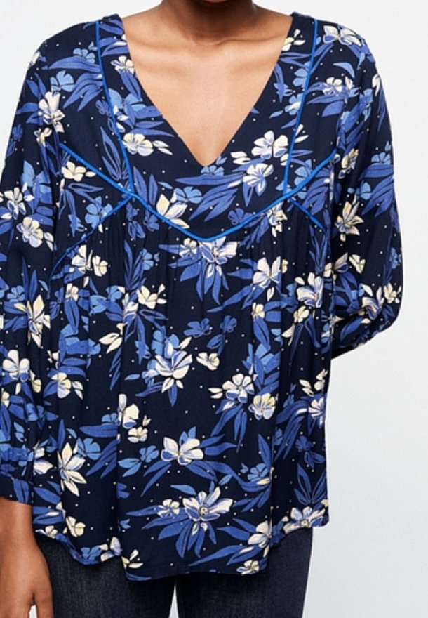 Květinová blůza z tmavě modré látky s bílými a modrými květy. Má hluboký V-výstřih a nabírané rukávy s modrým lemováním.