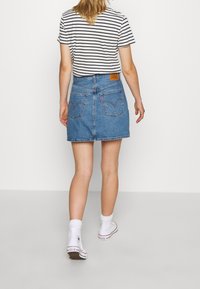 Der Jeansrock hat eine hellblaue Waschung, eine figurbetonte Taille, Taschen mit geschwungenen Nähten und ein Lederlabel auf der Rückseite. Kombiniert mit einem gestreiften T-Shirt.