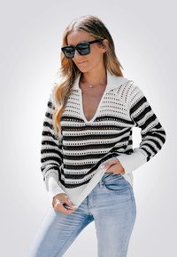 Suéter de punto a rayas con rayas horizontales en blanco y negro, un escote en V profundo y un cuello de canalé, combinado con jeans azul claro.