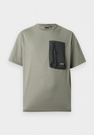 T-shirt vert olive à manches courtes avec une grande poche zippée noire sur la poitrine gauche, étiquetée "TAION MOUNTAIN WEAR".