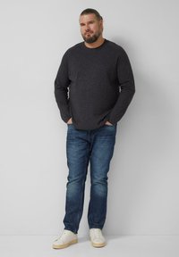 Dunkelgraues Langarmshirt mit rundem Ausschnitt, kombiniert mit mittelblauen Jeans und weißen Sneakers. Schlichtes Design, klassischer Schnitt.